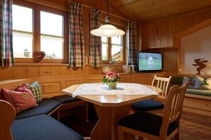 A cozy cabin interior with a dining table, chairs, a television, and a sofa. - Holiday apartment with 1 bedroom (Bad Hindelang)