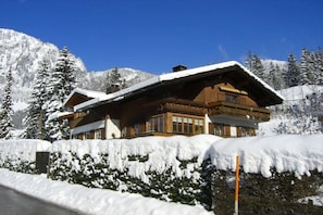 Un hotel de estilo chalet con fachada de madera, ventanas grandes y techo cubierto de nieve.