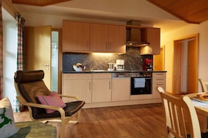 A cozy kitchen with wooden cabinets, a dining table, and a comfortable chair. - Holiday apartment with 1 bedroom (Bad Hindelang)