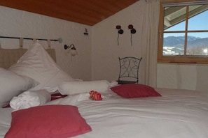 A bedroom with a bed, pillows, a metal headboard, a window with a view of mountains, and wall-mounted items. - Country House Schwab - Holiday Apartment Fellhorn (Sonthofen)