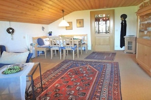 A cozy living room with a wooden ceiling, a dining area with a table and chairs, and a patterned rug on the floor. - Country House Schwab - Holiday Apartment Fellhorn (Sonthofen)