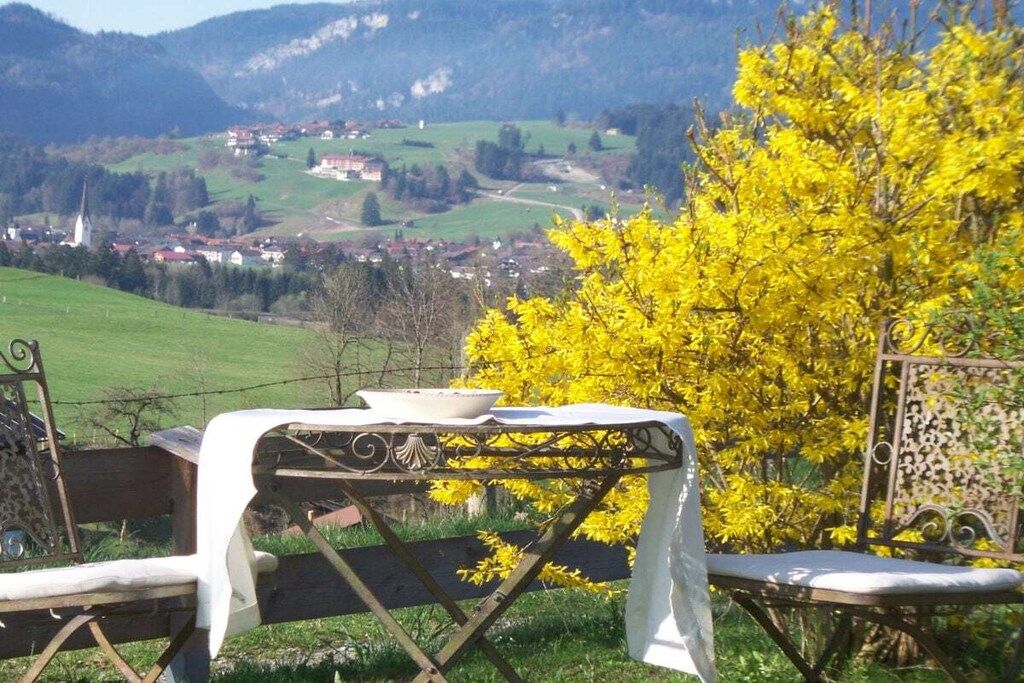 Ein Essbereich im Freien mit Tisch und Stühlen, Blick auf ein Dorf und ein gelb blühender Baum.
