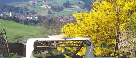 An outdoor dining area with a table and chairs, a view of a village, and a yellow flowering tree.