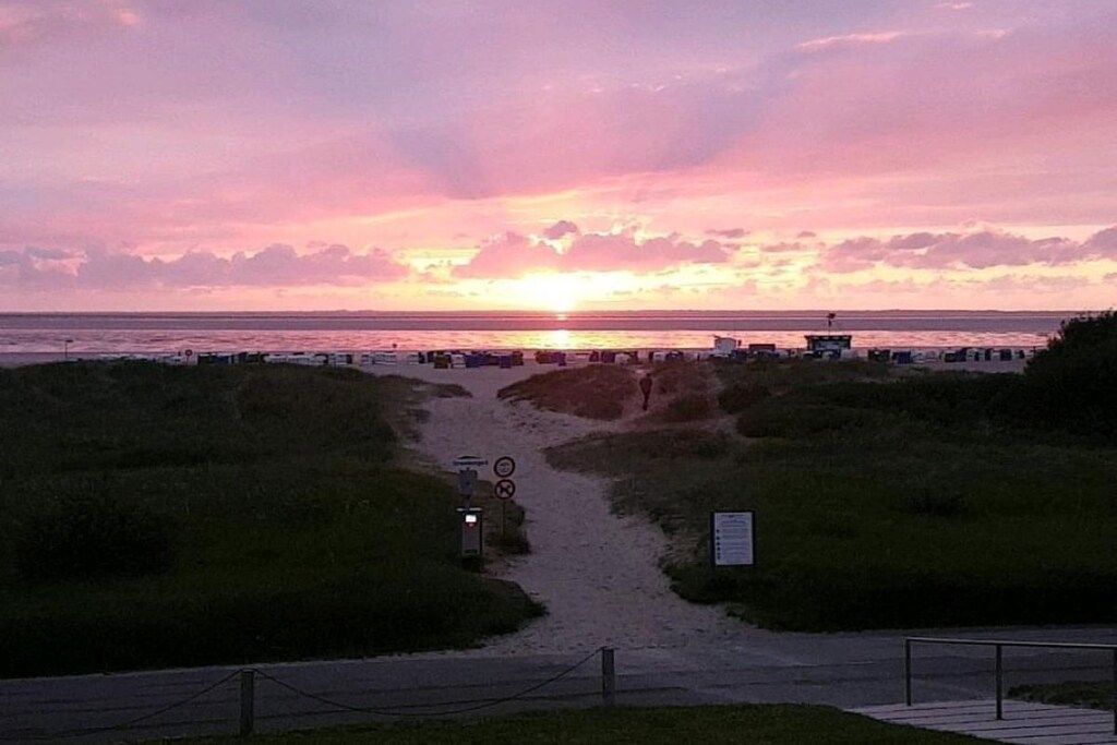 A sunset view from a beachside path with a sign and a bicycle.