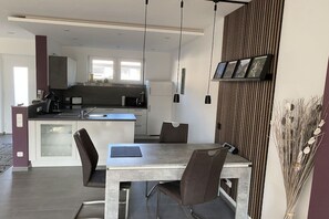 Eine moderne Küche mit einer zentralen Kochinsel, Pendelleuchten und einem Essbereich mit Tisch und Stühlen.