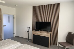 Ein modernes Hotelzimmer mit einem Flachbildfernseher, einem Holztisch, einem Stuhl und einem Bett mit weißer Bettdecke.