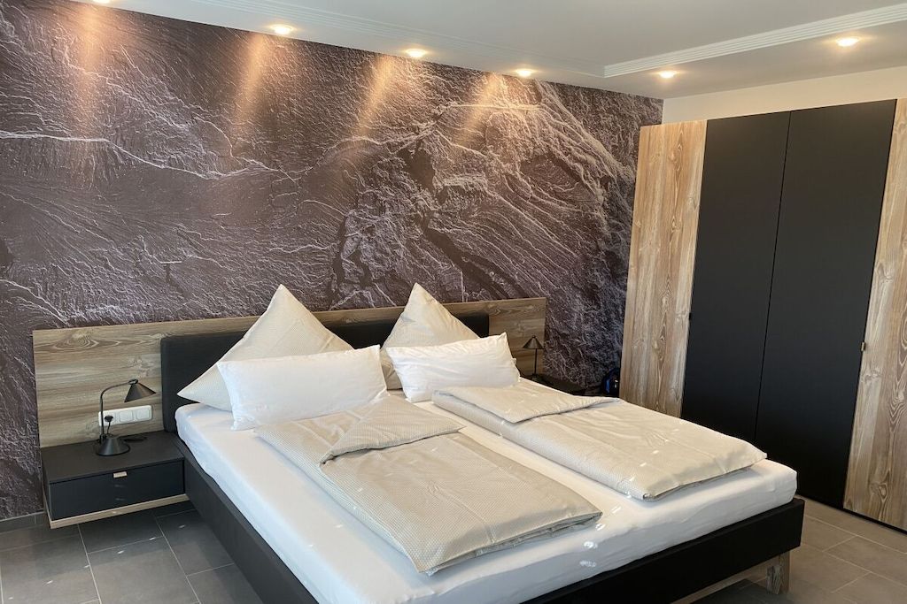 A modern bedroom with a marble-patterned wall, a wooden headboard, a black bed frame, and a nightstand with a lamp.