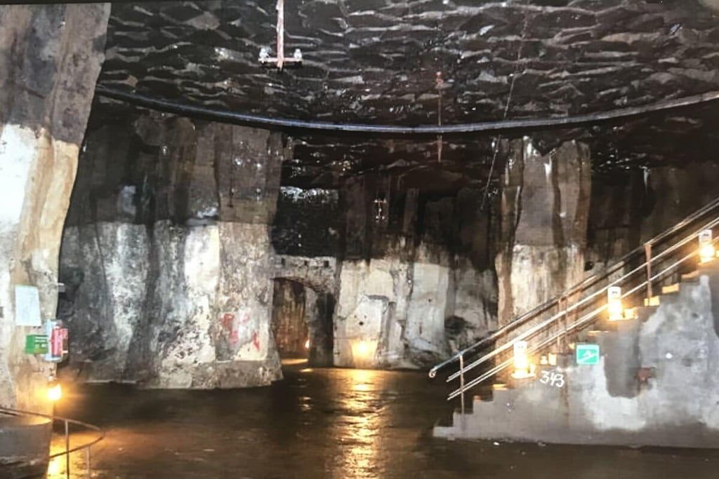Een donker, ondergronds gangpad met een waterpartij, een trap en een metalen hekwerk.