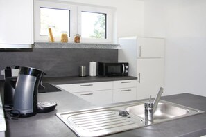 Eine moderne Küche mit einer Edelstahlspüle, einer Kaffeemaschine, einer Mikrowelle und einem Fenster über der Arbeitsfläche.
