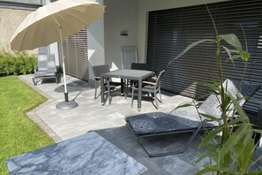 Eine Terrasse im Freien mit Tisch, Stühlen und einem großen Sonnenschirm.