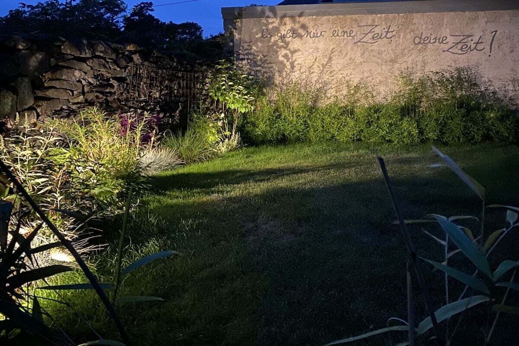 A stone wall with a sign that reads 'Es gibt mir eine Zeit, deine Zeit!' in a garden setting.