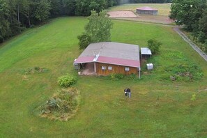 Ein eingeschossiges Holzhaus mit rotem Dach, umgeben von einer weiten Wiese und Bäumen.