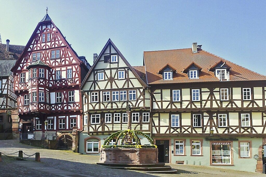 A traditional half-timbered building with a prominent tower and a fountain in front.