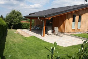 Ein Holzhaus mit überdachter Terrasse, Sitzgelegenheiten im Freien und einem gepflegten Rasen.