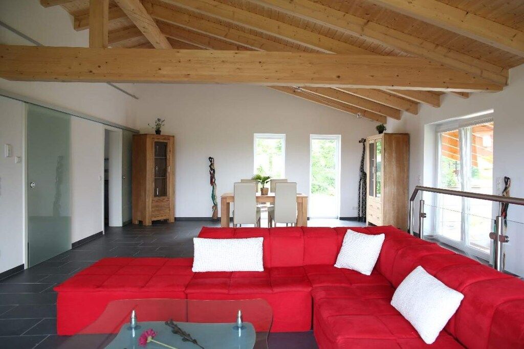 Un salon moderne avec un canapé d’angle rouge, une table basse en verre et un plafond en bois.