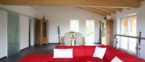 Una sala moderna con un sofá seccional rojo, una mesa de centro de vidrio y un techo de madera.