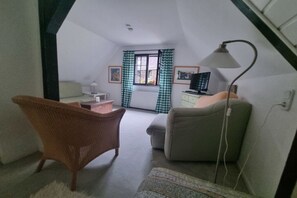 A small, cozy room with a high ceiling, a desk with a chair, a sofa, a lamp, and a television. - Carriage house to the old mill (Monschau)