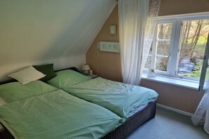 Een slaapkamer met een bed, een raam met gordijnen en uitzicht op het omliggende landschap.