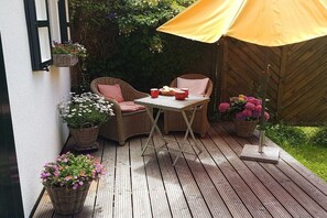 Een houten terras met rieten meubels, een tafel en een gele parasol.