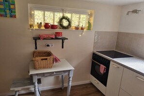 A kitchen with a window, a stove, and a small table with a basket. - Carriage house to the old mill (Monschau)
