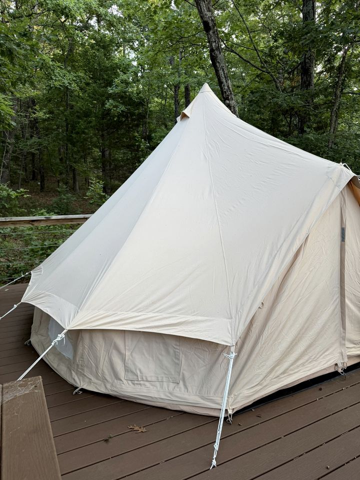 A large, white tent set up on a wooden deck surrounded by trees.