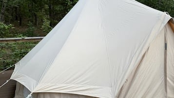 A large, white tent set up on a wooden deck surrounded by trees.