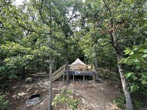 A cabin with a wooden deck and a covered seating area, surrounded by trees.