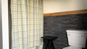 Une salle de bain avec des toilettes, un tabouret noir et un rideau de douche à carreaux.