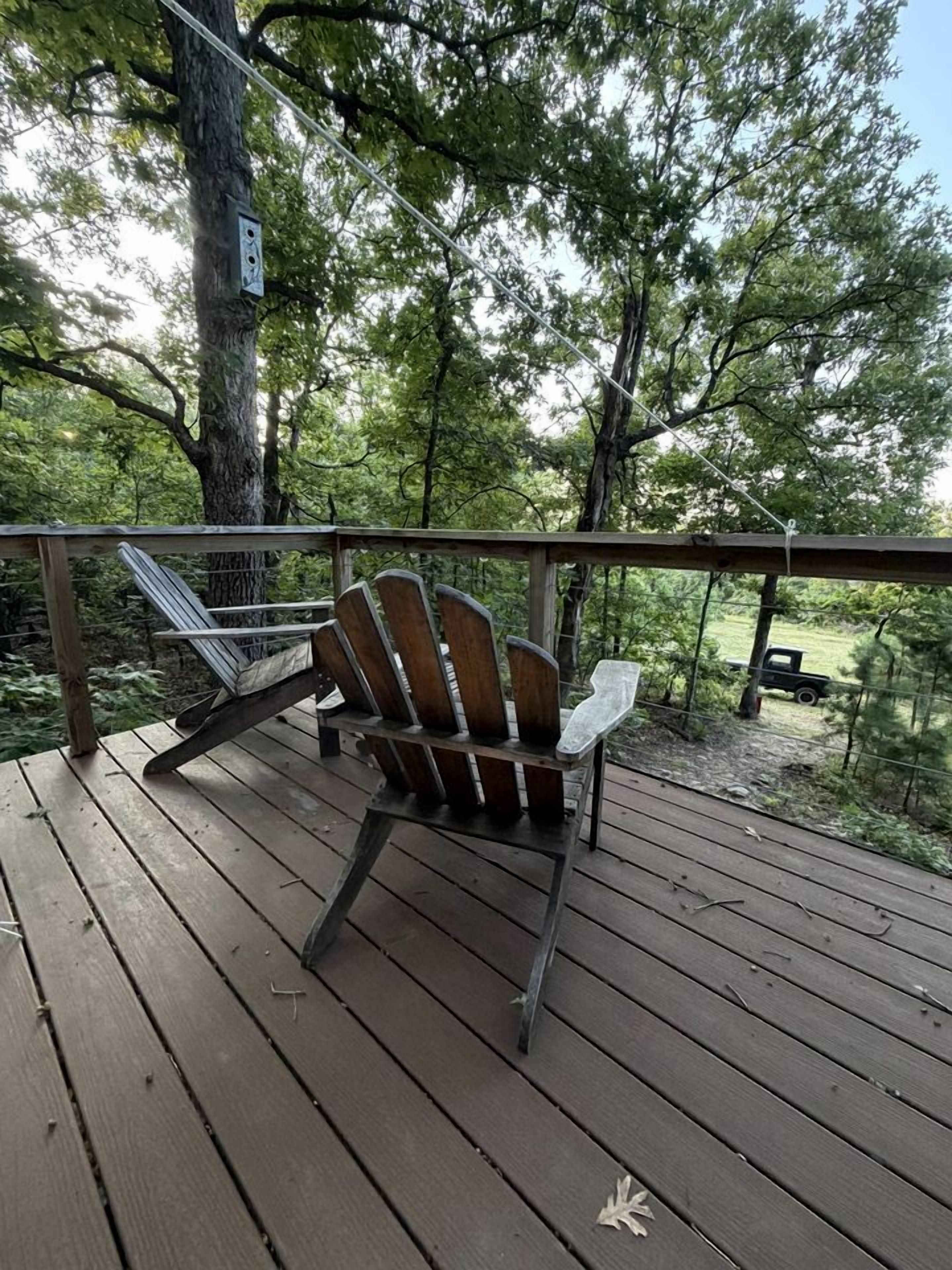A wooden deck with a chair and a railing overlooking a forested area.
