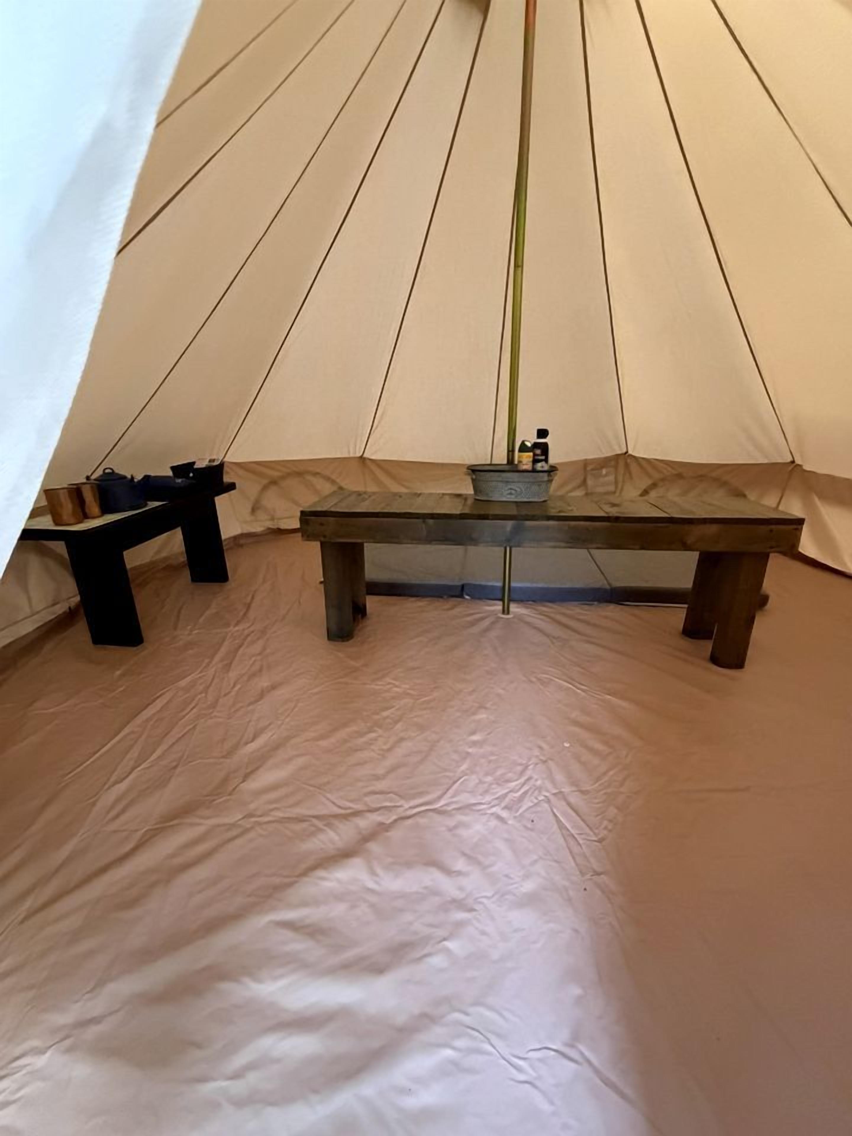 A tent interior with a central table, two benches, and a hanging light fixture.