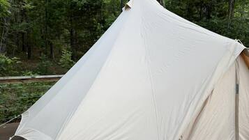 Une grande tente blanche est installée sur une terrasse en bois, entourée d’arbres.