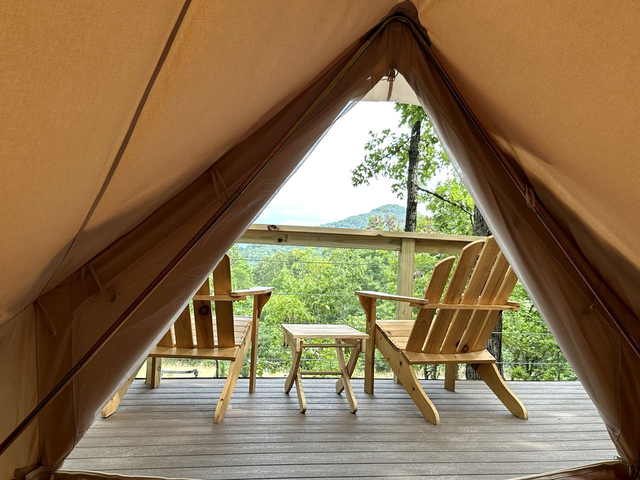 Ein Zelt mit einer Holzterrasse, zwei Holzstühlen und einem kleinen Tisch.