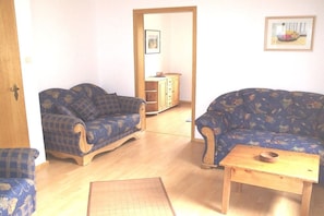 A living room with two blue patterned sofas, a wooden coffee table, and a small wooden side table. - Wolf with wood-burning stove (Zorge)
