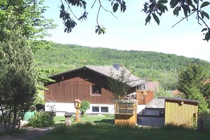 A wooden house with a sloped roof, a small shed, and a garden area with a tree and a bird feeder. - Wolf with wood-burning stove (Zorge)