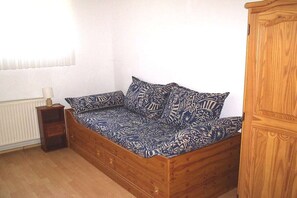 Een houten bed met beddengoed met een patroon in een kamer met een radiator en een houten kast.