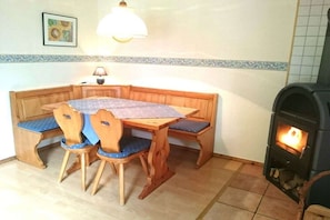 A corner room with a wooden table and chairs, a fireplace, and a wall-mounted lamp. - Wolf with wood-burning stove (Zorge)