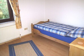A small, single-bed room with a wooden frame, a blue mattress, and a matching blue and white checkered duvet. - Wolf with wood-burning stove (Zorge)