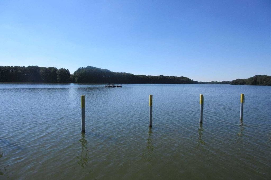 Un lac paisible, avec un bateau au loin et trois poteaux dans l’eau.