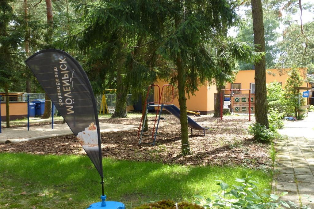 Een speeltuin met een glijbaan en klimconstructies, omringd door bomen en een gazon.