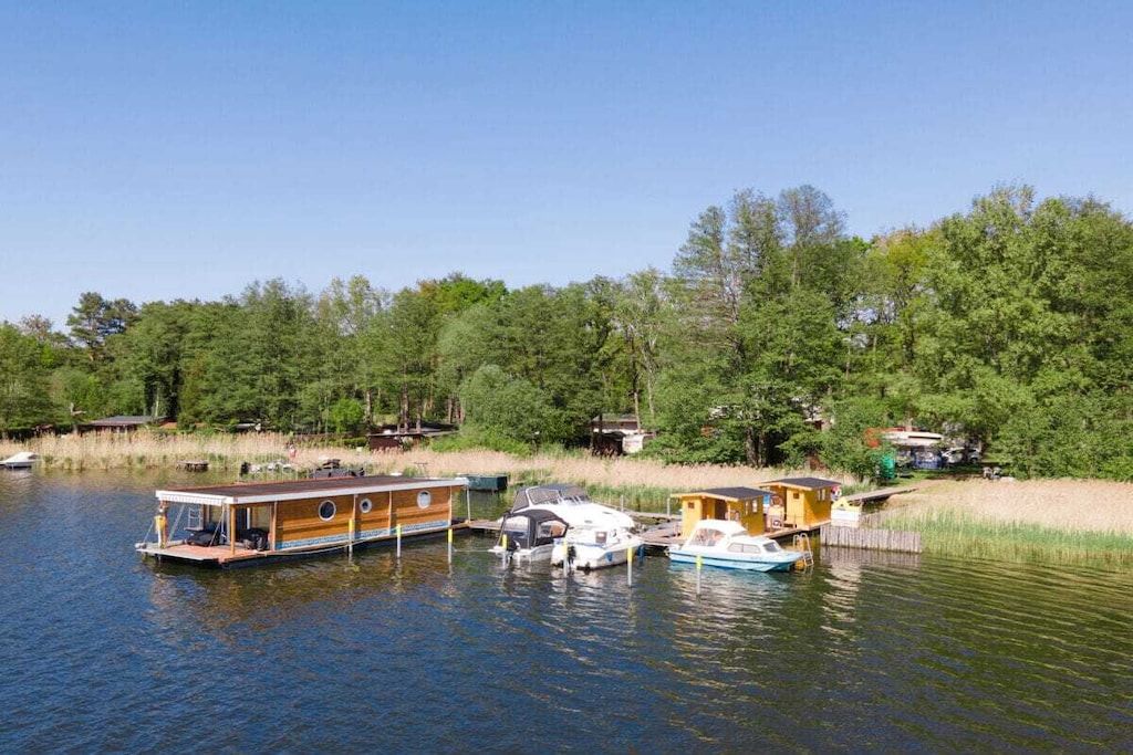 Un lac paisible où sont amarrées des maisons flottantes, entouré d’une forêt dense et surplombé d’un ciel dégagé.