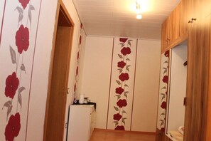 Une pièce avec un meuble en bois, un petit meuble blanc et une porte recouverte d’un papier peint à motifs floraux.
