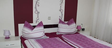 Un dormitorio con una cama, dos almohadas, una mesita de noche con una lámpara y un mueble auxiliar con una lámpara.