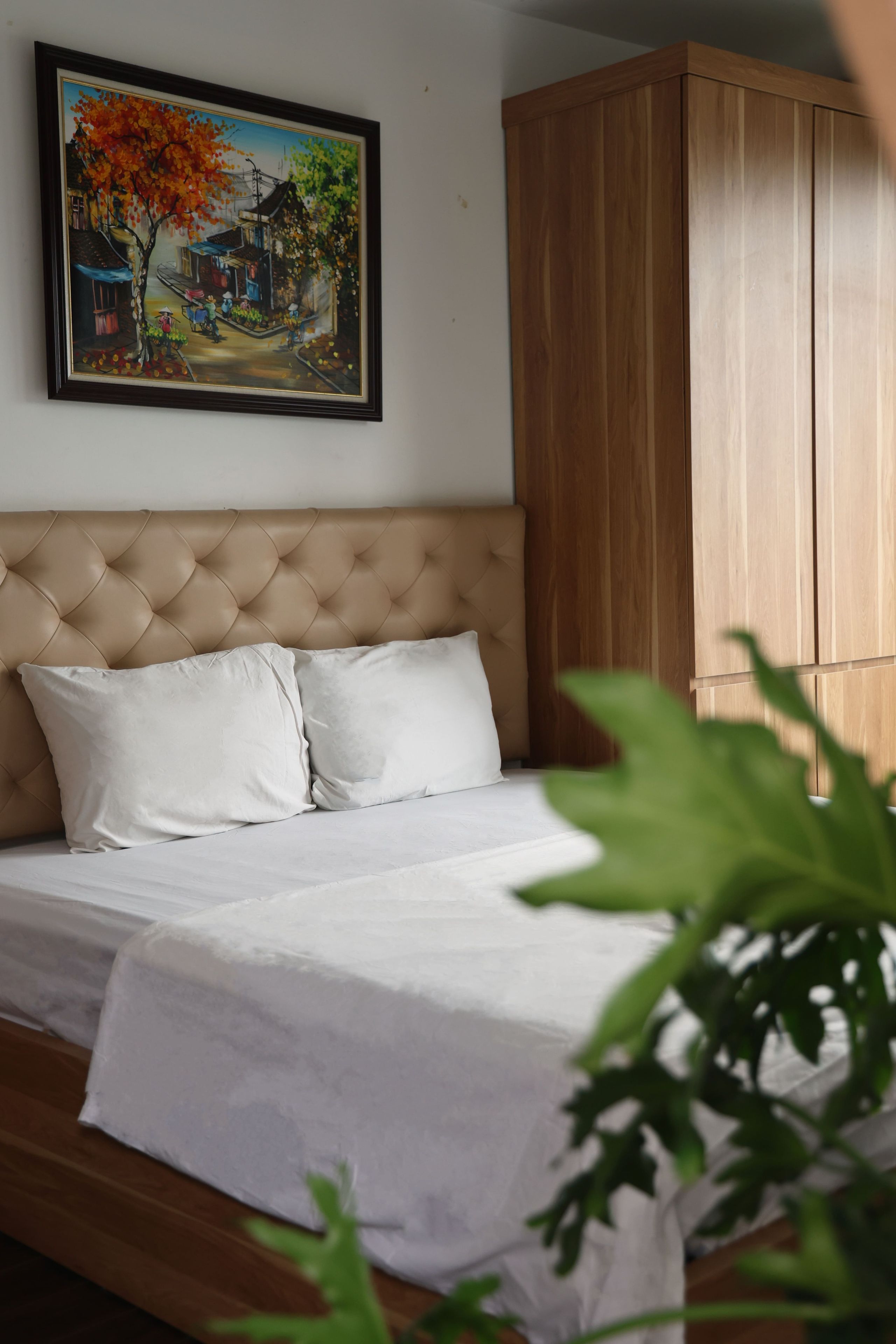A bedroom with a tufted headboard, a bed with white bedding, and a wooden wardrobe.