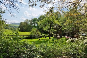 A lush garden with a swing set, a wooden bench, and a stone structure. - - Guesthouse Tenne ***** (Gersfeld)