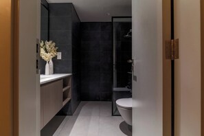 Een moderne badkamer met een donkere betegelde muur, een wit toilet en een douchehoek.