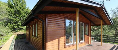 A wooden cabin with a deck, large windows, and a weather vane.