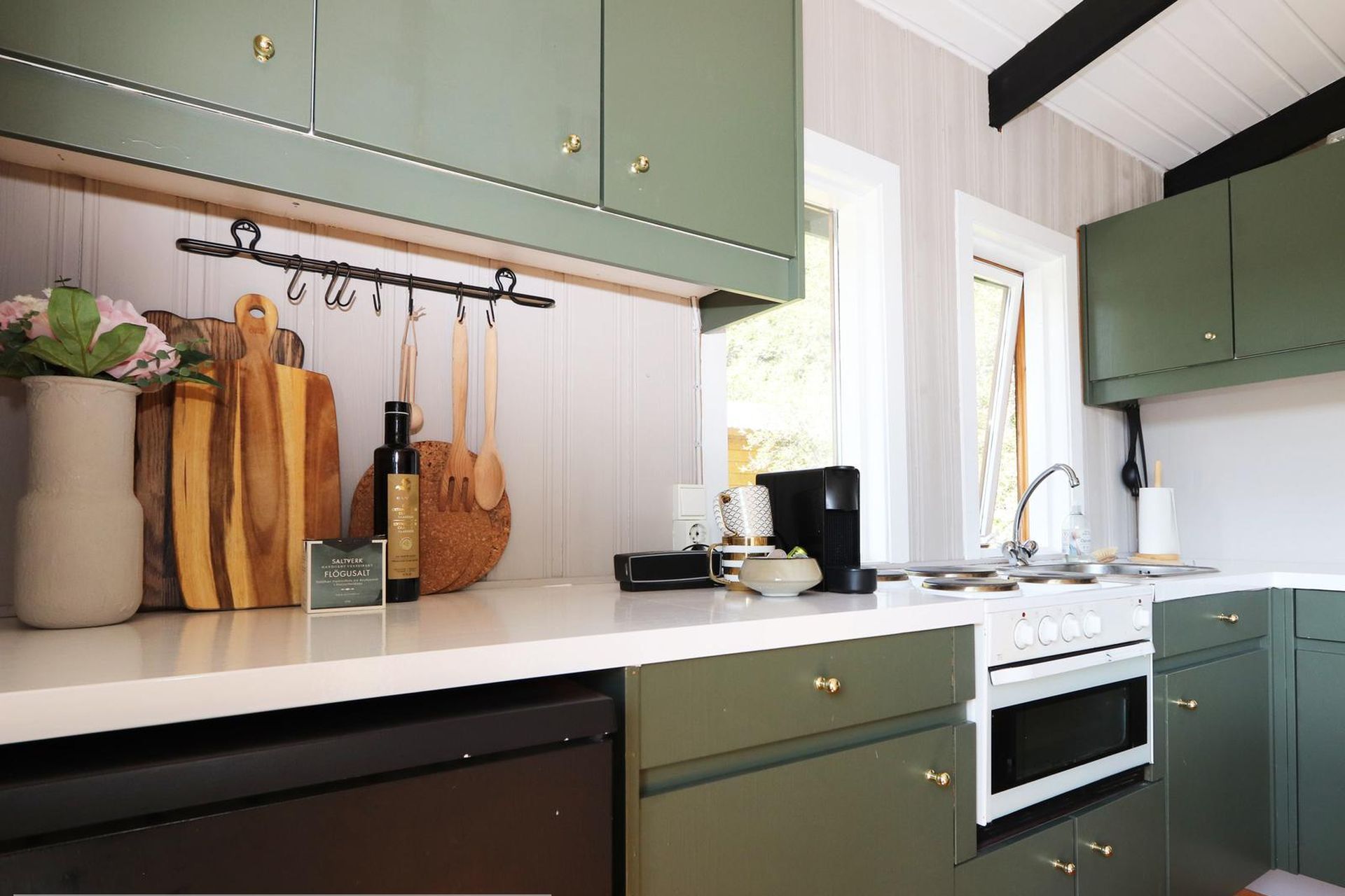 A kitchen with green cabinets, a white countertop, and various kitchen utensils and appliances.