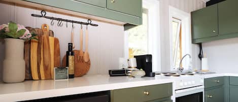 A kitchen with green cabinets, a white countertop, and various kitchen utensils and appliances.