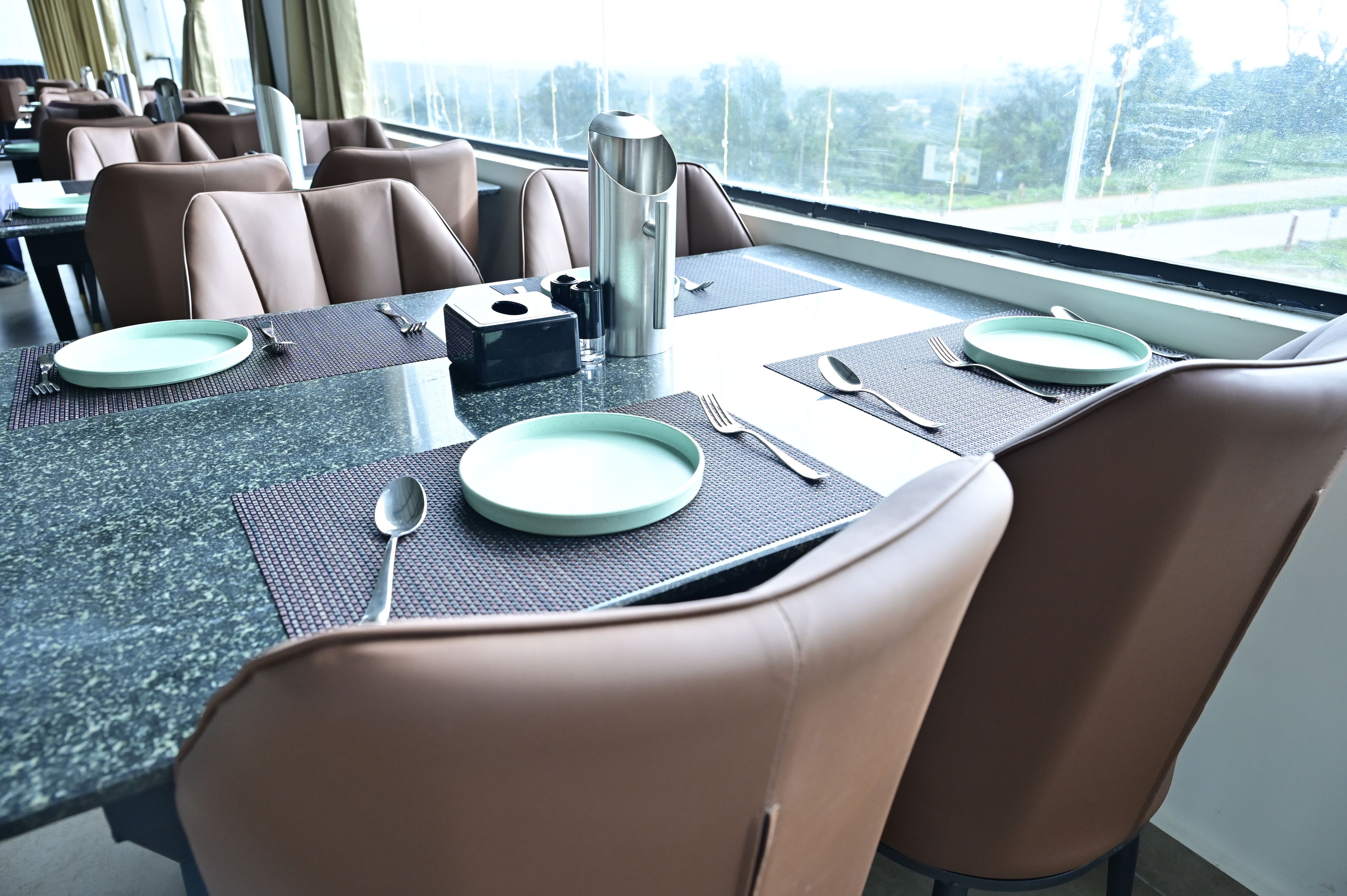 Un comedor con una mesa lista para dos personas, incluyendo platos, cubiertos y un termo.