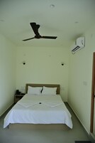 A hotel room with a bed, a ceiling fan, an air conditioning unit, and a nightstand.